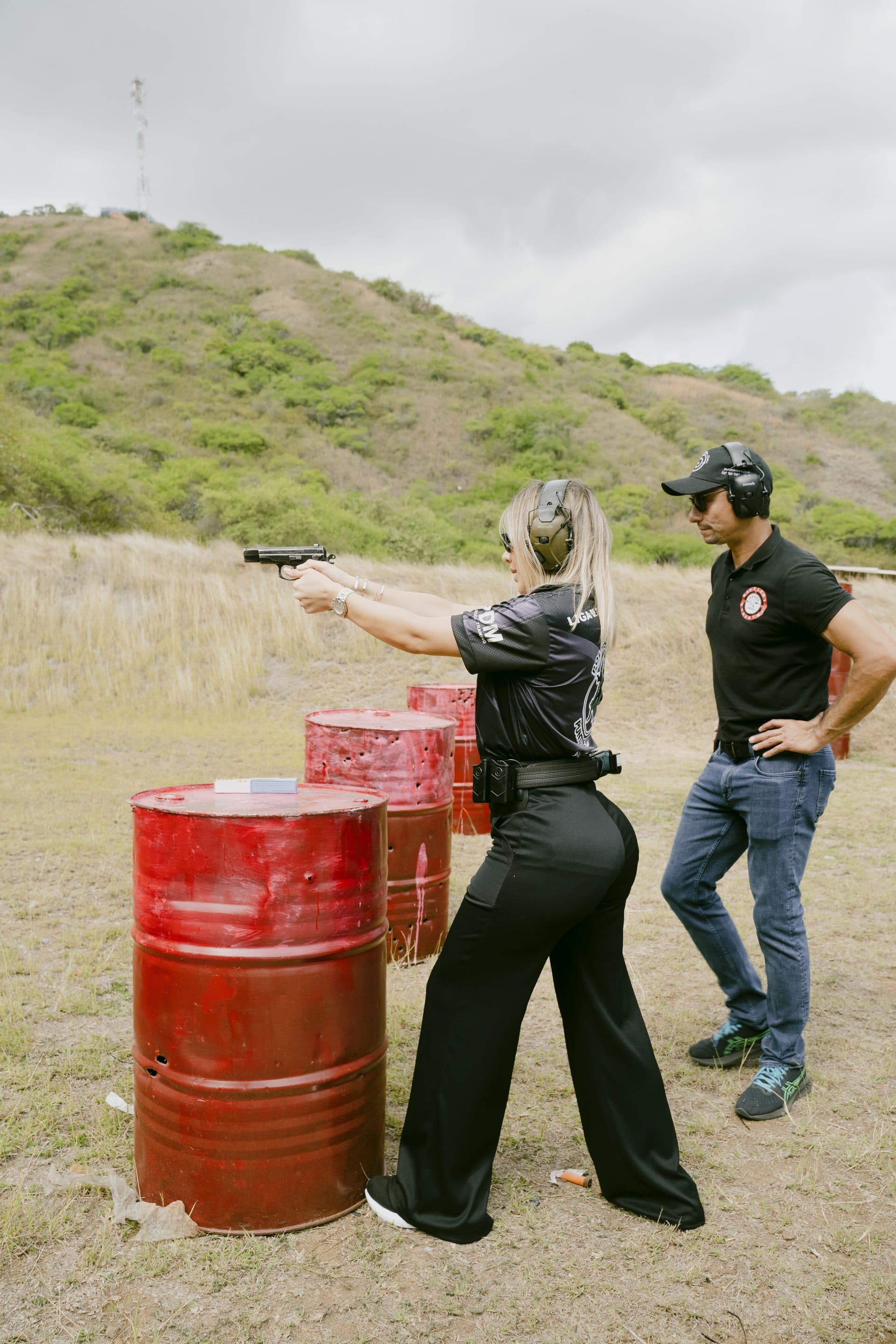 Participante disparando una pistola hacia los blancos con el instructor supervisando a su lado